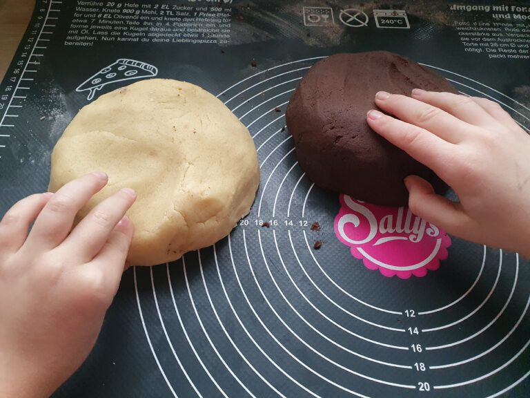 Ein heller und ein dunkler Keksteig mit jeweils einer Kinderhand die vom Teig mopsen.