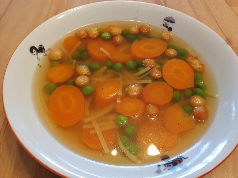 Ein Teller Suppe mit Möhren, Nudeln, Erbsen und Backerbsen.