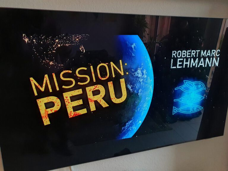 Ein Fernseher auf dem unsere Erde zu sehen ist darauf steht "Mission Peru Robert Marc Lehmann" Ein Logo mit einem Vogel, Blatt und Fisch ist zu sehen.