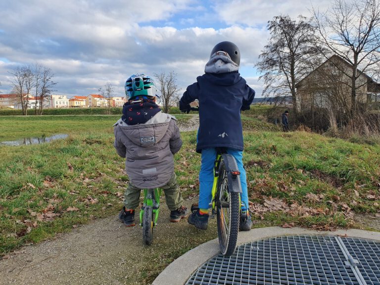 2 Kinder - Einer auf einem Fahrrad und einer auf dem Laufrad.