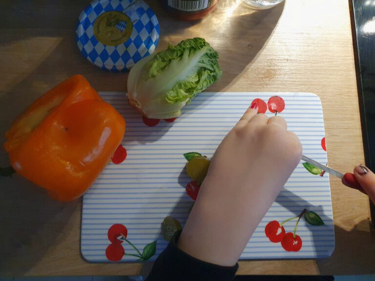 Eine Kinderhand die verschiedenes Gemüse schnibbelt.