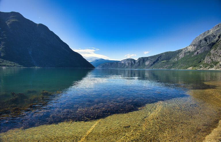 Blau türkises Wasser mit Bergen rechts und links. Der Himmel ist strahlend blau.