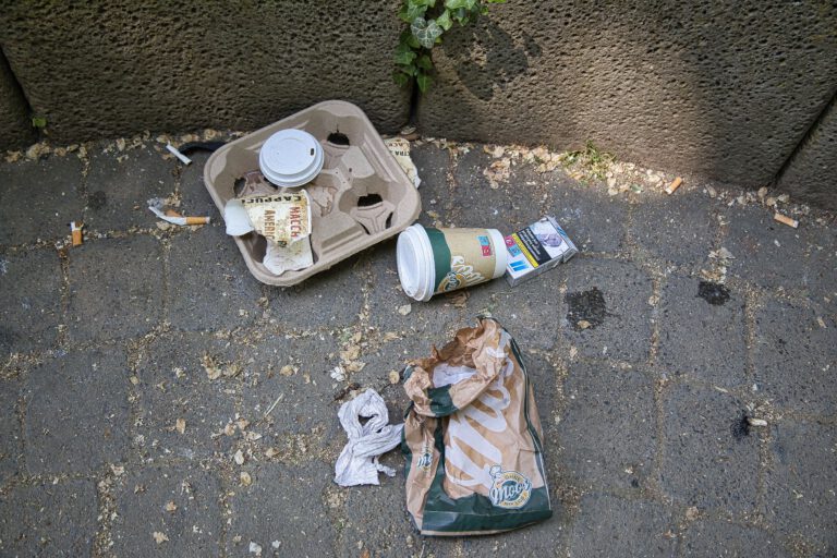 Plastik, Kaffeebecher, Zigarettenpackung, Bäckertüten und Zigarettenstummel auf dem Boden.