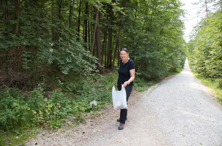 Ich, in schwarz gekleidet, mit einer Mülltüte und einer Müllzange im Wald.