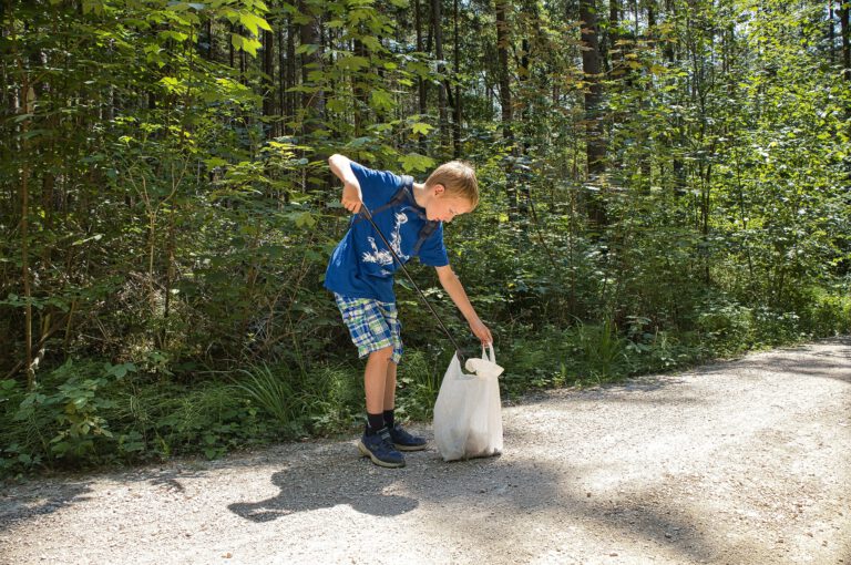 Ein Kind mit einer Mülltüte und Müllzange im Wald.