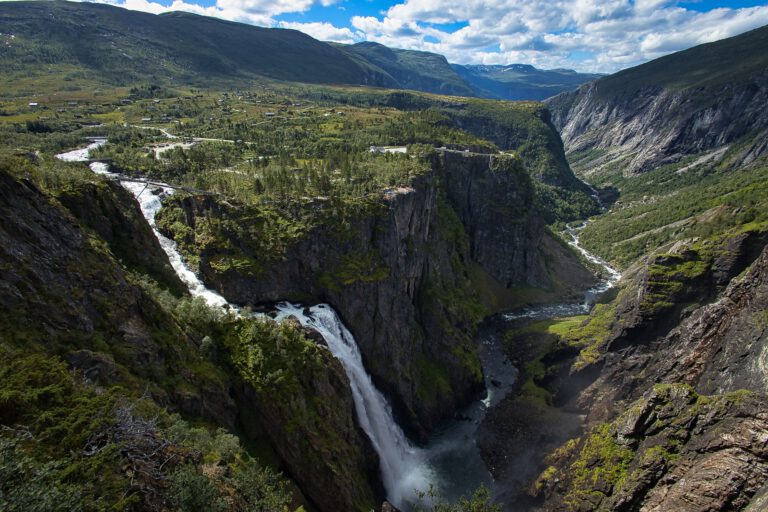 Ein großer Wasserfall rauscht den Hang hinab. Drumherum ist alles grün und bergig. Der Himmel ist blau mit weißen Wolken.