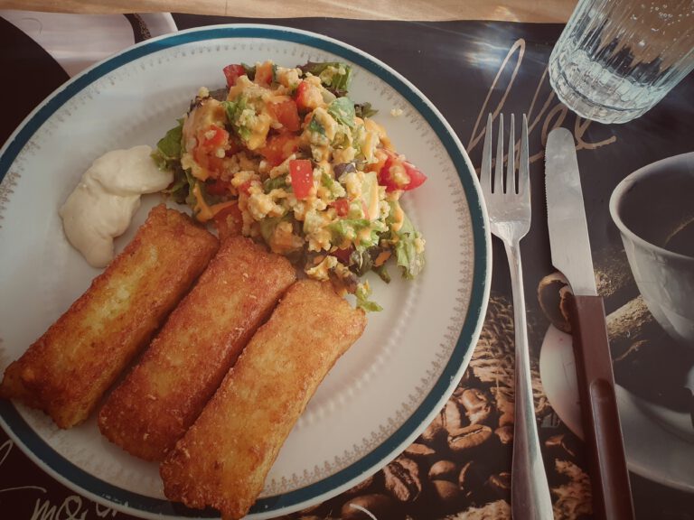 Ein Teller mit Salat und Kartoffelsticks. Außerdem Messer, Gabel und ein Glas Wasser.