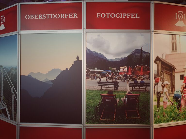 Ein Aussteller mit verschiedenen Bildern von Bergen. Oben drüber steht "Oberstdorfer Fotogipfel"