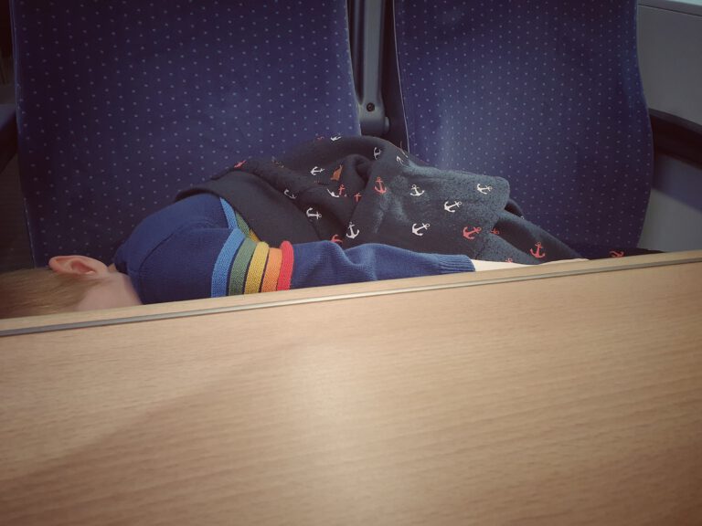Ein kleines Kind liegt über zwei Sitze im Zug und schläft.