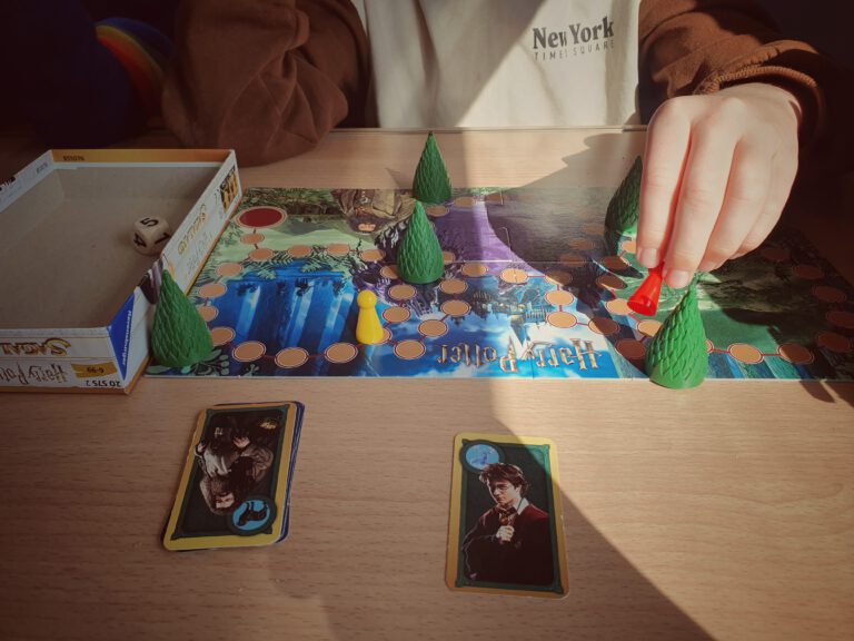 Auf einem Tisch im Zug ist ein Brettspiel mit Bäumen und Figuren aufgebaut. Ein Kind zieht sein Püppchen weiter.