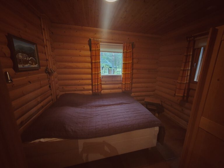 Ein kleiner Raum mit Holz ausgekleidet. 2 kleiner Fenster und ein Bett.