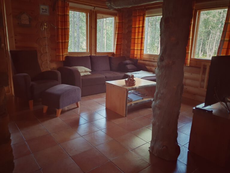 Eine Couch und ein Sessel hinter einem kleinen Holztisch. Rechts im Bild ist ein Holzstamm.